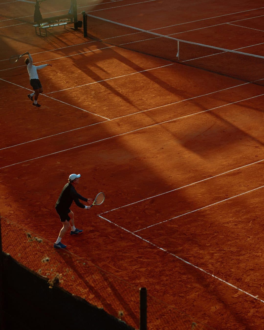 Two players mid-rally on a sunlit clay court