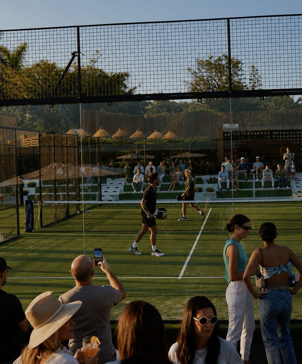 Guests gathered courtside during a golden-hour padel match