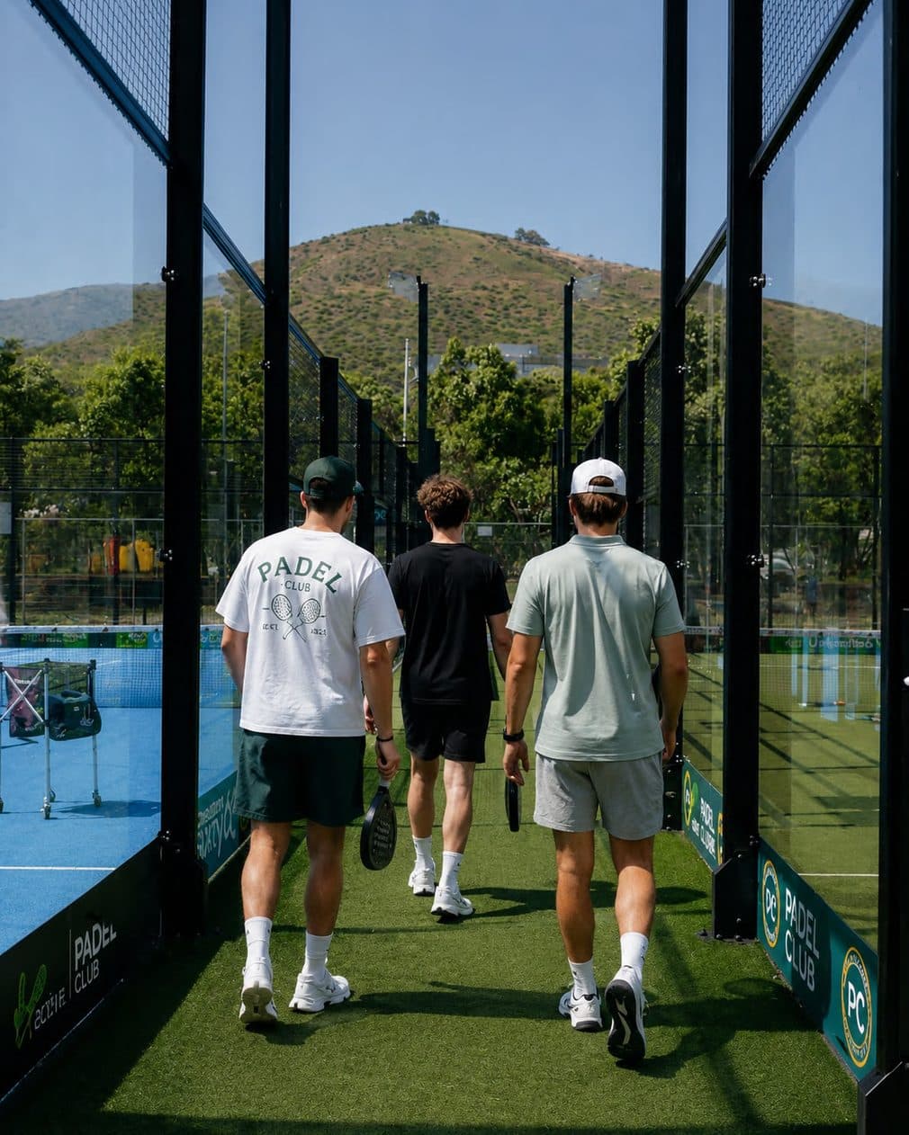 Three friends with rackets walking between glass padel courts
